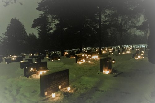 Hautamuistomerkkejä, joiden edessä palavia kynttilöitä lumen päällä talvihämyssä kuvattuna.